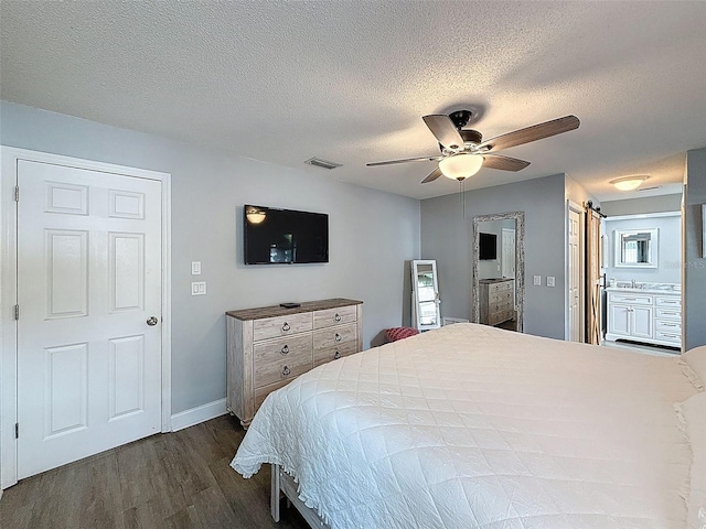 bedroom featuring dark wood finished floors, visible vents, a textured ceiling, and a barn door