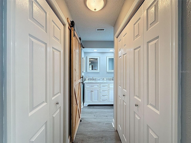 corridor with visible vents, dark wood finished floors, a barn door, a textured ceiling, and a sink