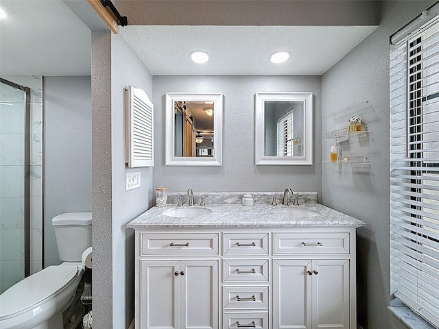 full bath with double vanity, a textured ceiling, toilet, and a sink