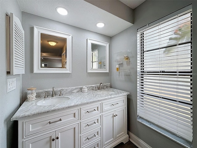 full bath featuring a sink, double vanity, and a textured wall