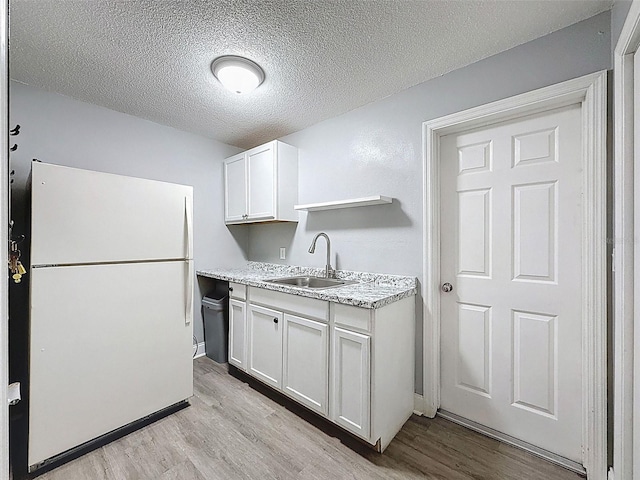 kitchen with a sink, light wood-type flooring, freestanding refrigerator, white cabinets, and open shelves