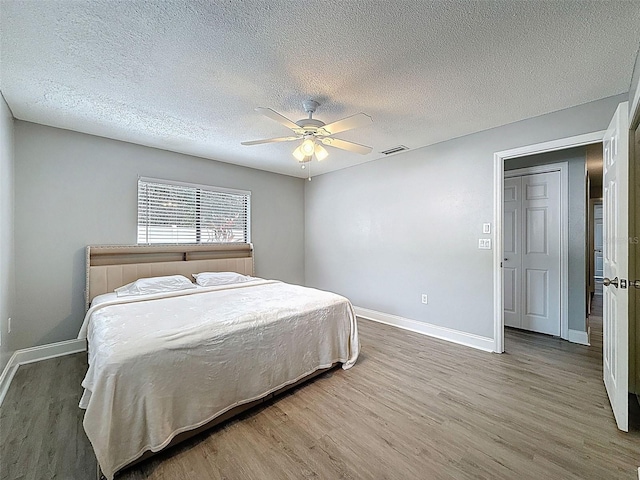 bedroom with visible vents, a textured ceiling, wood finished floors, baseboards, and ceiling fan