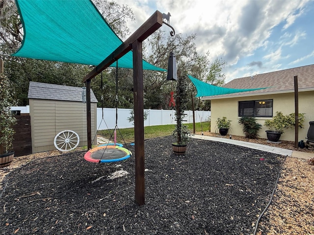 view of playground featuring a fenced backyard, an outbuilding, and a storage shed