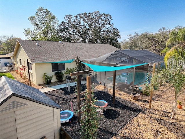 rear view of property with stucco siding, fence, glass enclosure, roof with shingles, and a pool