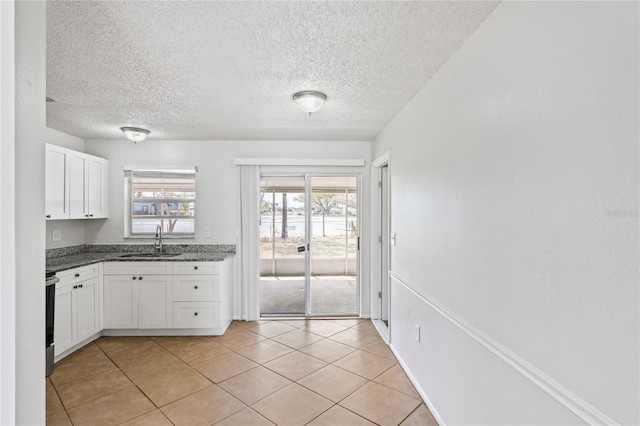 kitchen featuring white cabinetry, dark stone counters, light tile patterned flooring, a textured ceiling, and a sink