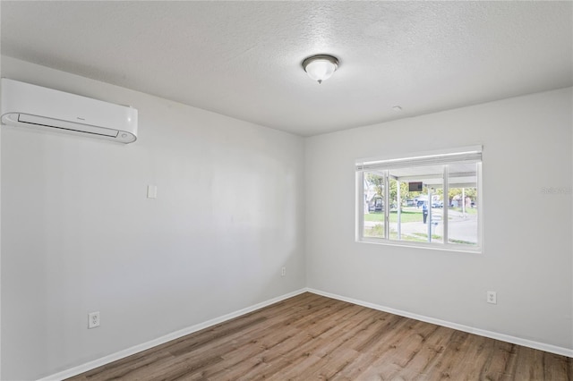 unfurnished room with an AC wall unit, wood finished floors, baseboards, and a textured ceiling