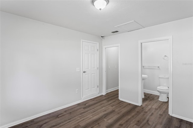 unfurnished bedroom with visible vents, baseboards, attic access, wood finished floors, and ensuite bath