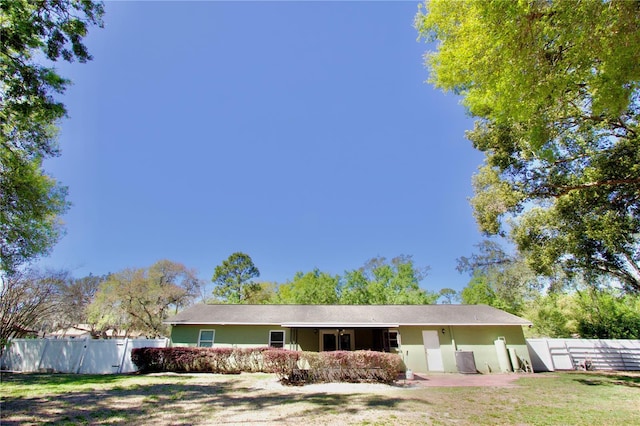 rear view of house featuring stucco siding, a lawn, and fence