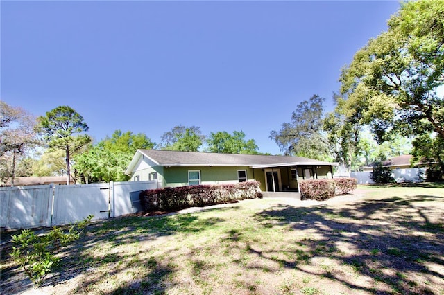 rear view of house featuring a gate, fence, a sunroom, stucco siding, and a lawn