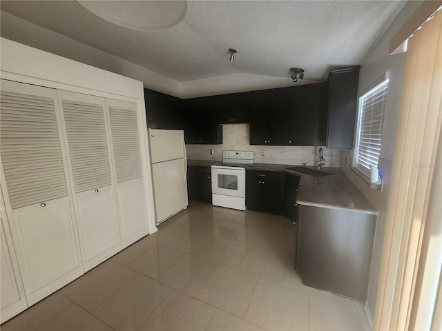 kitchen featuring dark cabinetry, white appliances, a sink, vaulted ceiling, and tasteful backsplash