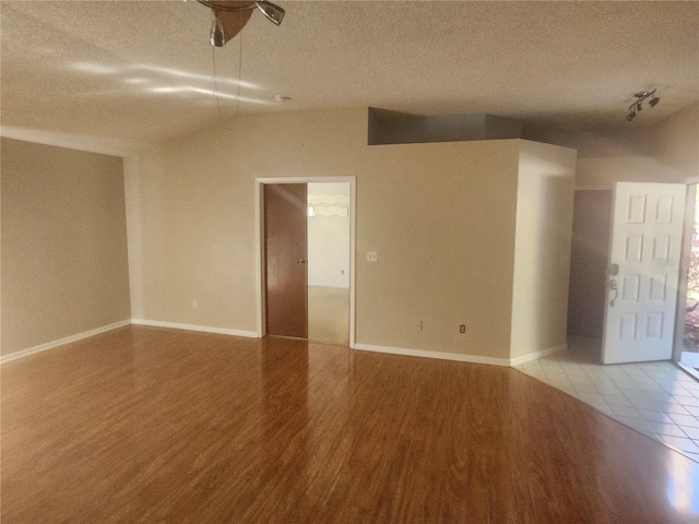 empty room with a textured ceiling, lofted ceiling, and wood finished floors