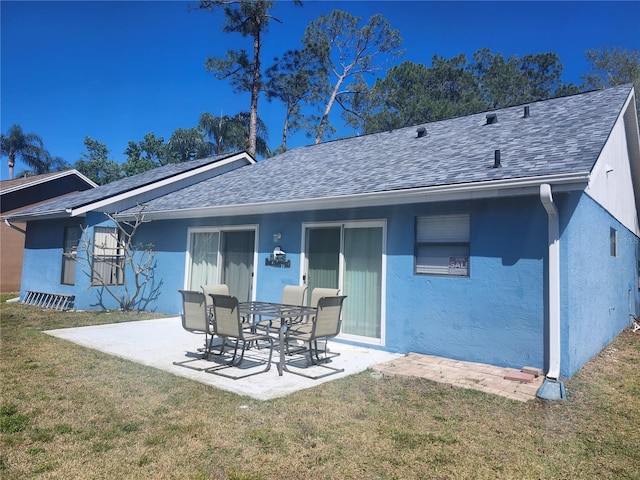back of house featuring stucco siding, a patio, a lawn, and a shingled roof