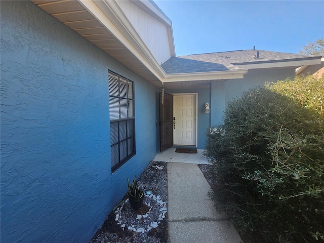 view of exterior entry featuring stucco siding and roof with shingles
