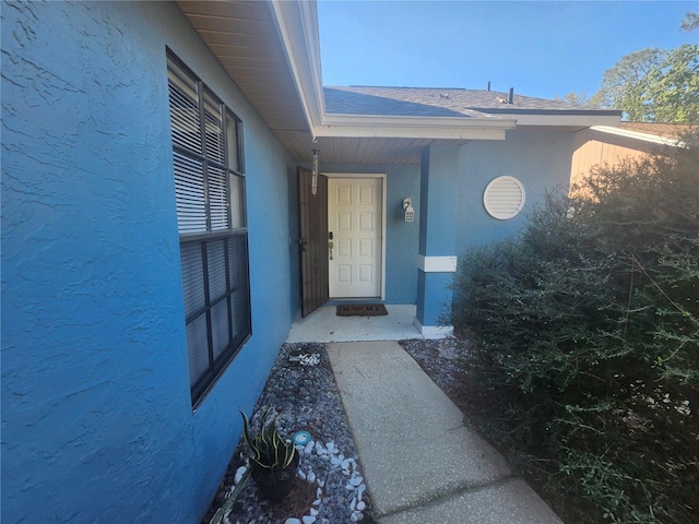 doorway to property with a shingled roof and stucco siding