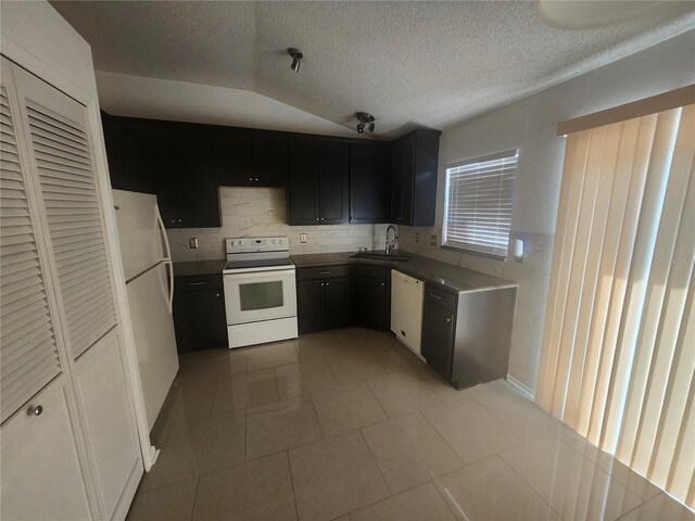 kitchen with a sink, a textured ceiling, dark cabinetry, white appliances, and light tile patterned floors