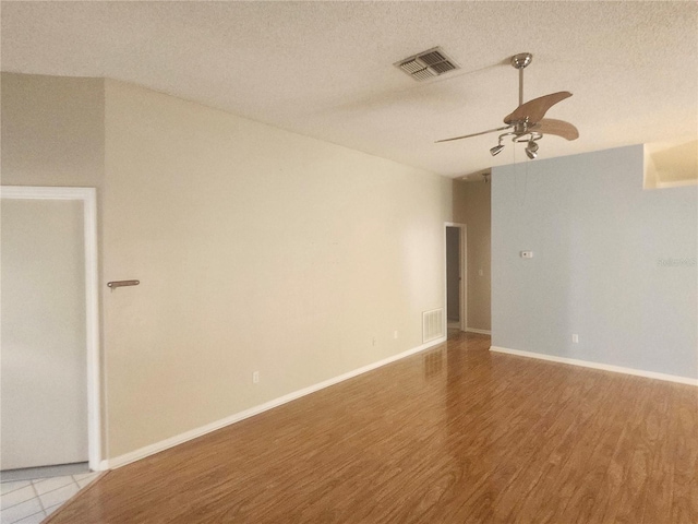 empty room with a textured ceiling, wood finished floors, visible vents, and ceiling fan