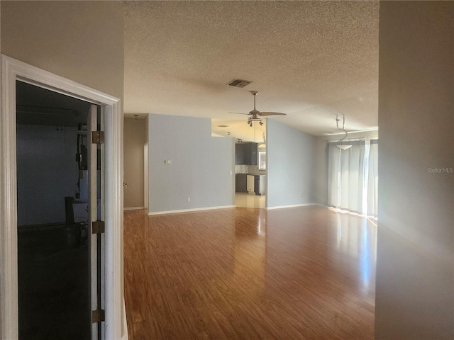 unfurnished room featuring visible vents, vaulted ceiling, wood finished floors, a textured ceiling, and a ceiling fan