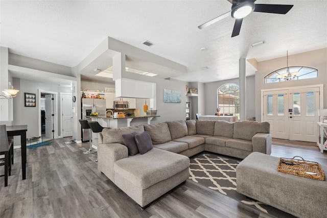 living room featuring ceiling fan with notable chandelier, wood finished floors, and visible vents