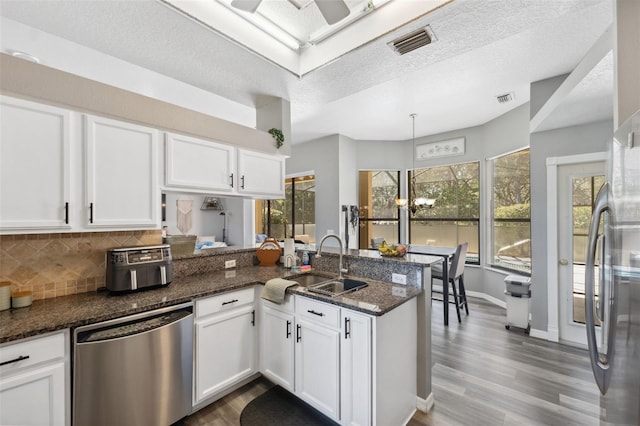 kitchen with visible vents, a peninsula, stainless steel appliances, white cabinetry, and a sink