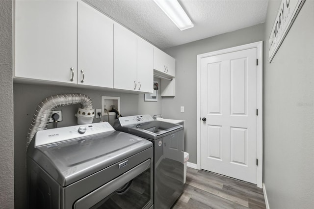 laundry area featuring a textured ceiling, washing machine and dryer, wood finished floors, cabinet space, and baseboards