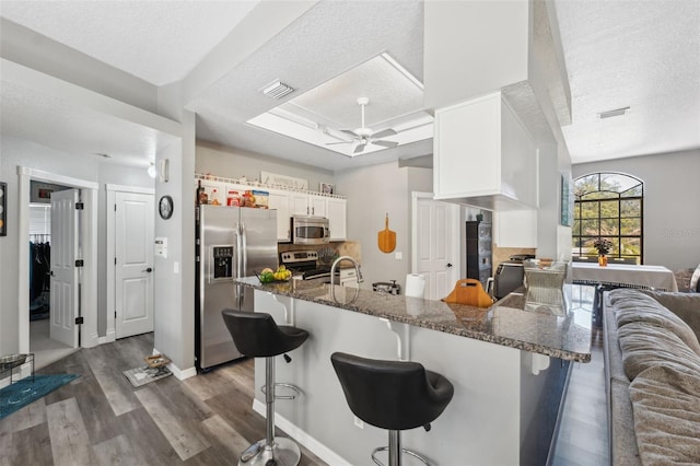 kitchen featuring a kitchen bar, visible vents, dark wood-type flooring, white cabinetry, and stainless steel appliances