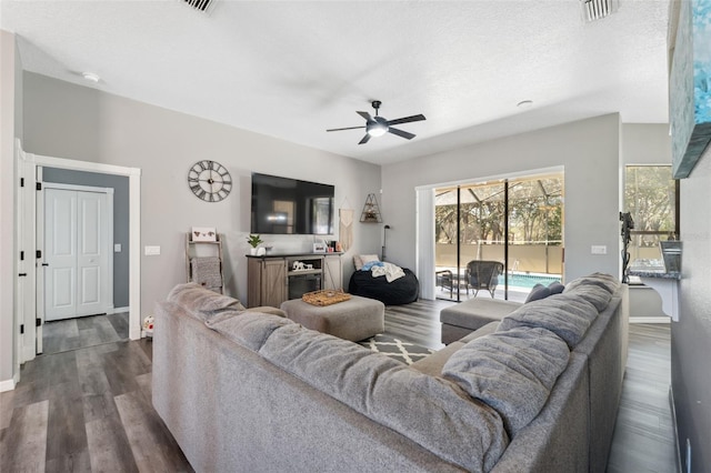 living room with dark wood-style floors, visible vents, baseboards, ceiling fan, and a textured ceiling