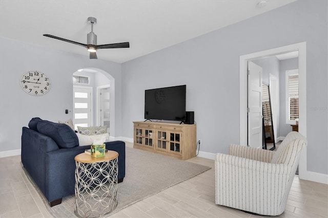 living room with ceiling fan, baseboards, arched walkways, and wood finished floors