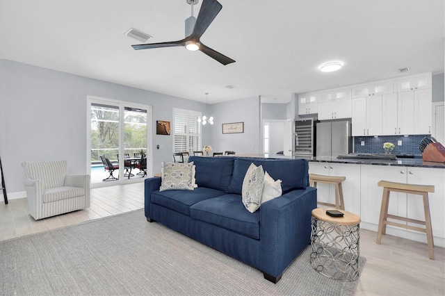 living room featuring light wood-style floors, ceiling fan with notable chandelier, and visible vents