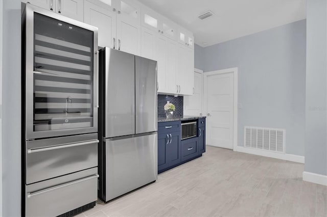 kitchen with visible vents, freestanding refrigerator, glass insert cabinets, white cabinetry, and backsplash