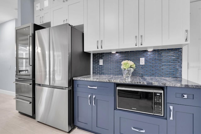 kitchen featuring light stone countertops, backsplash, freestanding refrigerator, and white cabinetry