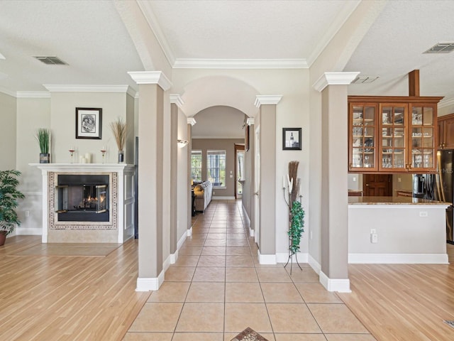 foyer featuring visible vents, arched walkways, a tile fireplace, and decorative columns