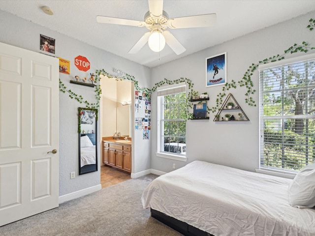 bedroom featuring a sink, ensuite bath, baseboards, light colored carpet, and ceiling fan