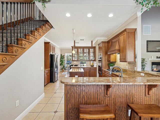 kitchen with crown molding, premium range hood, light tile patterned floors, a peninsula, and stainless steel appliances