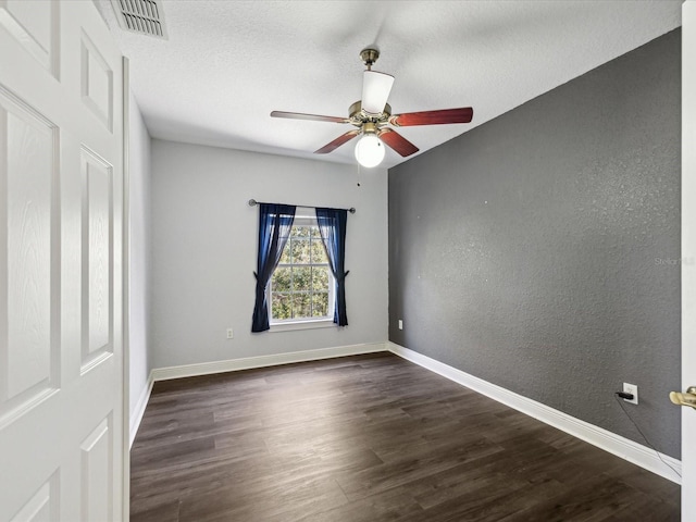 empty room featuring visible vents, dark wood-type flooring, a textured ceiling, baseboards, and a textured wall