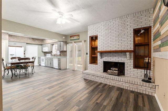 living area featuring a fireplace, baseboards, a ceiling fan, and wood finished floors