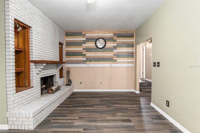 unfurnished living room with a brick fireplace, wood finished floors, and baseboards