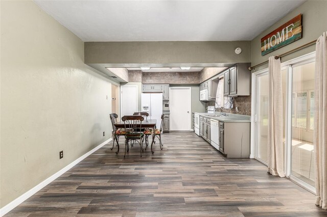 kitchen featuring tasteful backsplash, baseboards, dark wood-style floors, white appliances, and a sink