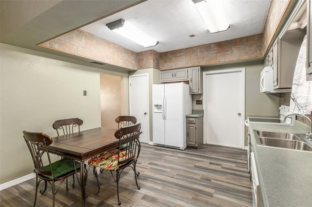 kitchen with white appliances, wood finished floors, gray cabinetry, and a sink