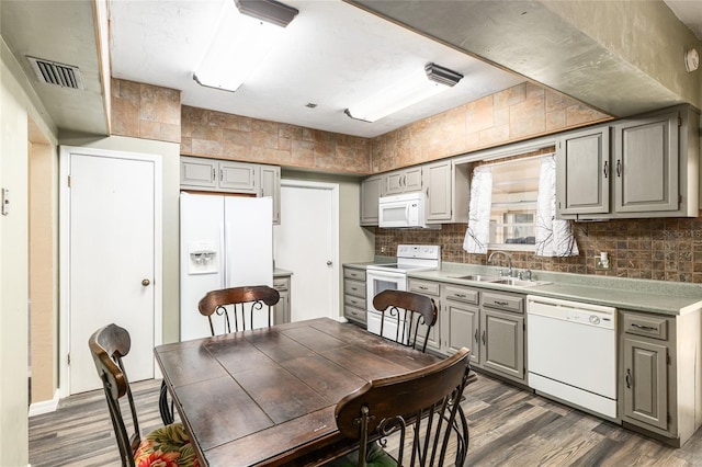 kitchen with gray cabinets, a sink, wood finished floors, white appliances, and decorative backsplash