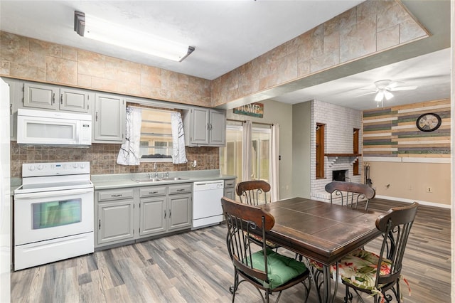 kitchen featuring white appliances, a brick fireplace, light wood-style flooring, and gray cabinets