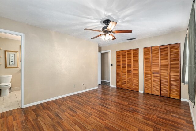 unfurnished bedroom with wood finished floors, visible vents, two closets, and connected bathroom