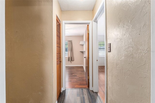 corridor with baseboards, dark wood finished floors, and a textured wall