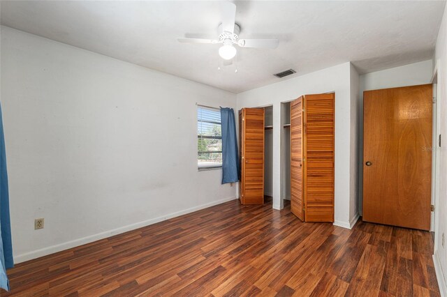 unfurnished bedroom featuring baseboards, wood finished floors, visible vents, and multiple closets