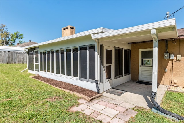 exterior space featuring fence, a lawn, a chimney, and a sunroom