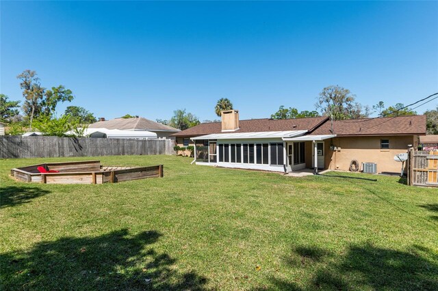 view of yard featuring central AC unit, a sunroom, a fenced backyard, and a garden