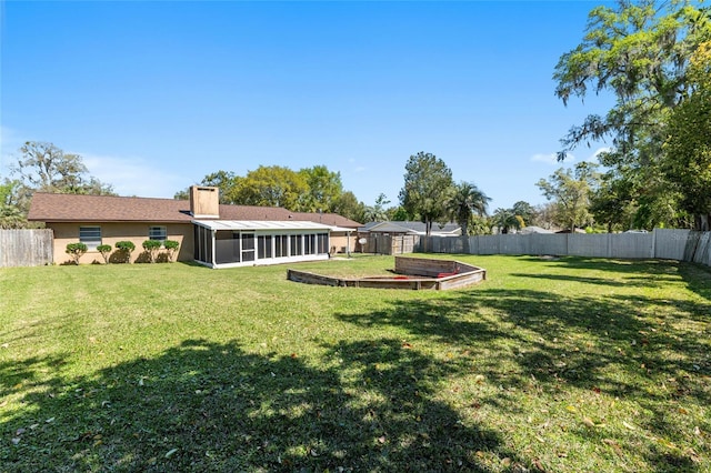 view of yard featuring a garden, a fenced backyard, and a sunroom