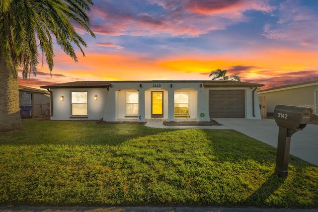 view of front of property with a yard, a garage, driveway, and stucco siding