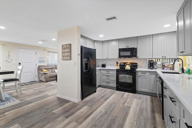 kitchen with light wood finished floors, gray cabinetry, black appliances, and a sink