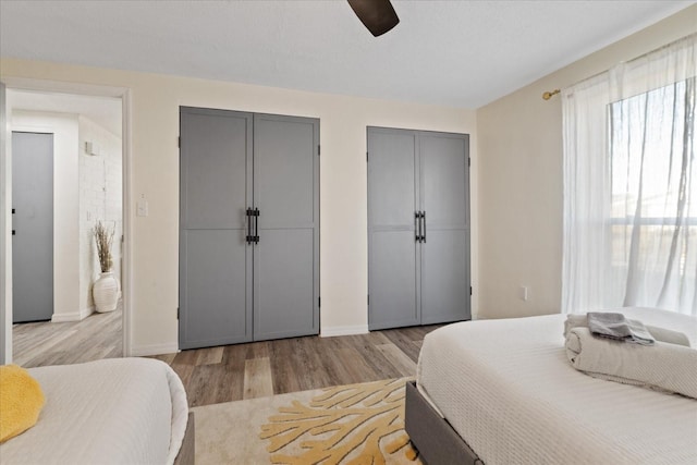 bedroom featuring baseboards, light wood-style floors, multiple closets, and a ceiling fan