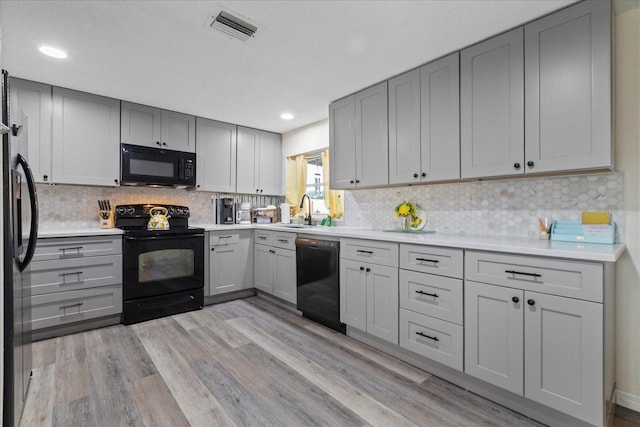 kitchen with visible vents, gray cabinets, black appliances, light countertops, and light wood-type flooring